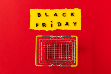 Black friday basket. Top view of yellow torn paper sheet and black friday text on red background. With shopping cart.