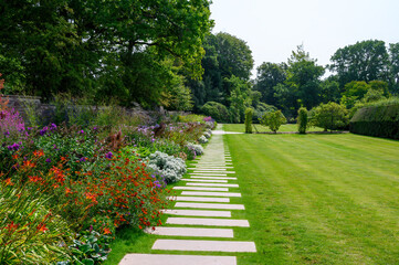 Fototapeta premium Beautiful garden pathway lined with colorful flowers in a sunny park during springtime