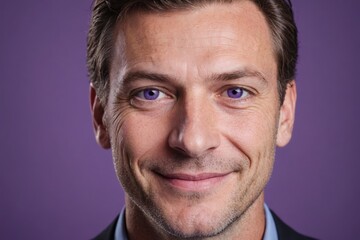 Fototapeta premium Full framed very close face portrait of a smiling 40s caucasian man with violet eyes looking at the camera, studio shot,violet background.