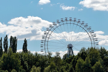Fototapeta premium A Beautiful Ferris Wheel Set Against A Vibrant Blue Sky With Fluffy Clouds. This Image Captures The Essence Of Leisure And Adventure In Nature.