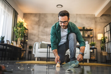 Fototapeta premium Adult man clean up broken glass on the floor of a modern living room