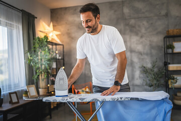 Adult man ready to iron clothes on board in modern home interior
