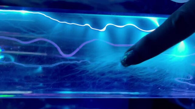 Finger touches transparent glass tube with blue neon gas discharging in plasma