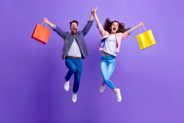 Full body side view young couple two friends family man woman wear casual clothes together hold shopping package bags jump high isolated on plain purple background. Black Friday sale buy day concept