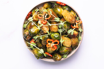 Tasty vegan low carb dish with fried Brussels sprout, peas greens, hot Habanero pepper and soy sauce on white marble background close up. Healthy diet food concept.