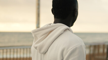 Back view of handsome athlete man walking down the boardwalk, feeling tired after street workout