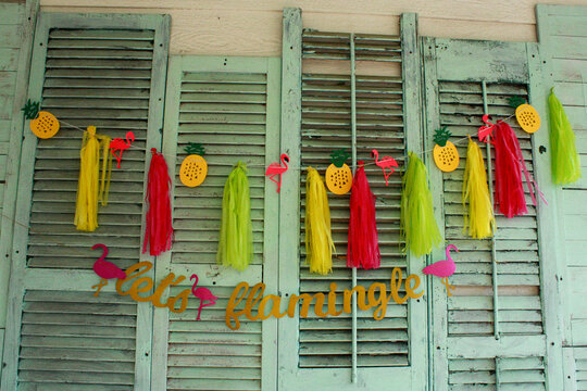 Let's flamingle sign with pink, yellow, and green streamers, hangin on light blue old, wooden shutters