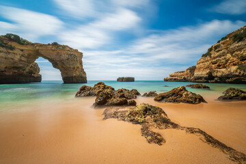Idyllic Algarve beach with a natural rock arch and blurred turquoise waters, long exposure,...