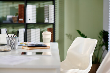 Workspace desk featuring coffee cup, stationery items, and office documents with bookshelf and plant in background creating an organized professional setting