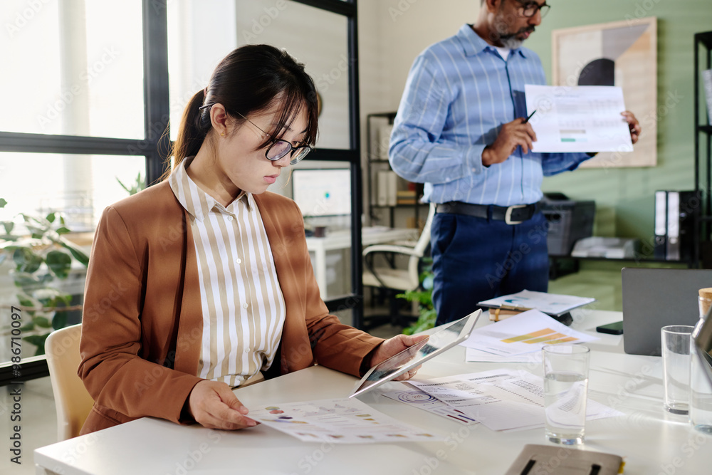 Fototapete Woman and man in office colaborating on documents and charts Shuffling papers, discussing reports, using various gadgets and technology while working on a project in bright workspace