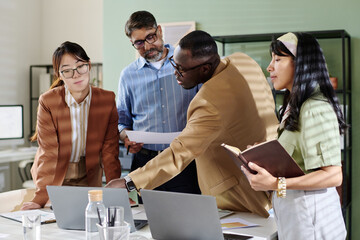 Colleagues sharing ideas and discussing plans in modern office room. Diverse team engaging in collaborative work environment focusing on team project