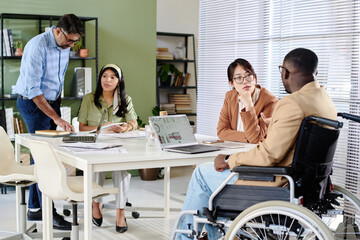 Group of colleagues working together in office, including person in wheelchair, engaging in...