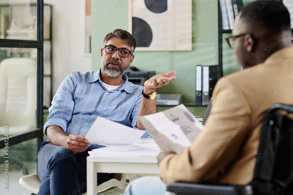 Poster Two professionals discussing business strategy while reviewing documents in modern office setting with contemporary decor and glass partitions