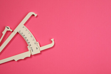 Plastic body fat caliper on pink background, top view. Space for text