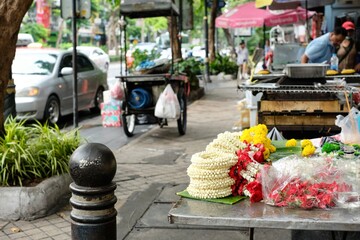 Naklejka premium A stall selling floral garlands, and other food carts and street vendors setting up shop at the entrance to the morning wet market at Soi 20 in Silom - Bang Rak, Bangkok