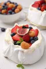 Pavlova cake (meringue dessert) with whipped cream, fresh berries, fig and mint on table, closeup