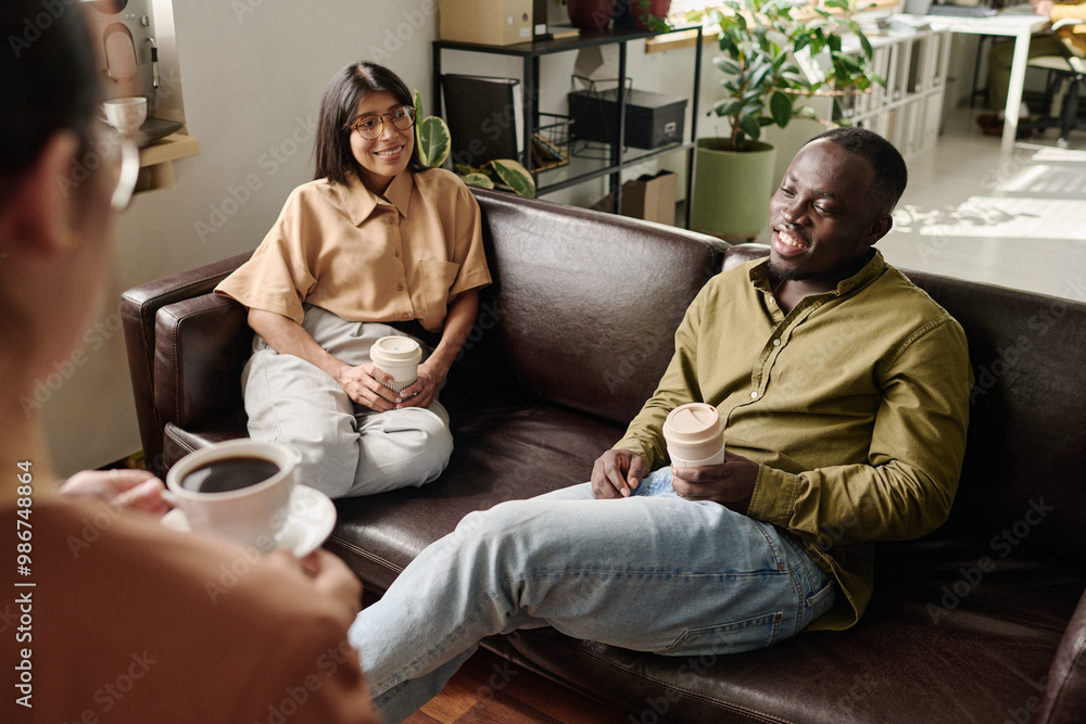 Poster people sitting on comfortable couches enjoying coffee and casual conversation in a modern office env