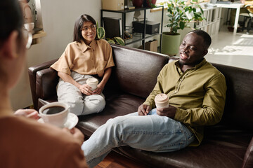 Obraz premium People sitting on comfortable couches enjoying coffee and casual conversation in a modern office environment with plants and natural light streaming in through large windows
