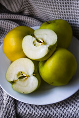 Ginger Gold apples on a plate against a cloth background, shown whole and cut in half