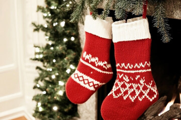 Festive red knitted Christmas stockings hanging by a fireplace decorated with a holiday tree