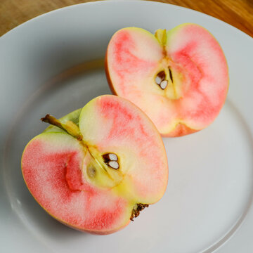 A Hidden Rose apple on a plate, cut in half to show the distinctive red and white inner flesh