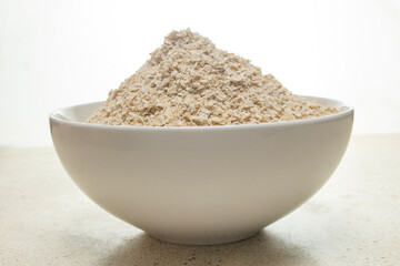 front view of whole oats, or quick oat flakes in a white bowl with a white marble bottom