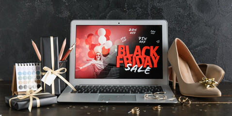 Laptop with Black Friday sale advertisement, shoes, jewellery and gift boxes on dark wooden table