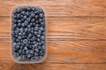 Plastic container with fresh blueberry on wooden background