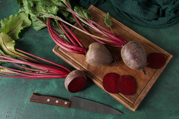 Cutting board with bunch of fresh cut beetroots and knife on green table