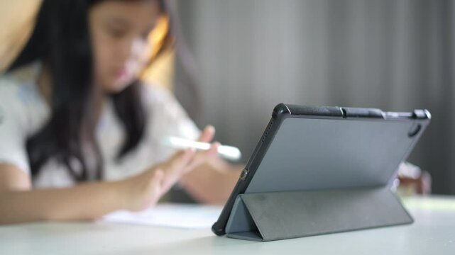 closeup tablet with blur asian child or kid girl study online class to reading paper or learning from home school by computer laptop or people studying learn by technology education to swinging pen