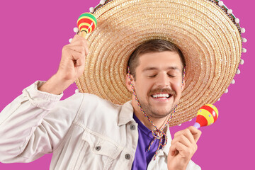 Young Mexican man in sombrero and with maracas on magenta background