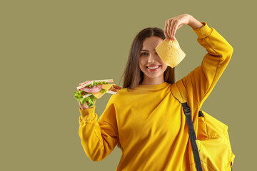Female student with tasty sandwich on green background