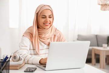 Young Muslim woman working with laptop at table in office