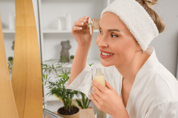 Beautiful woman applying serum near mirror in bathroom, closeup