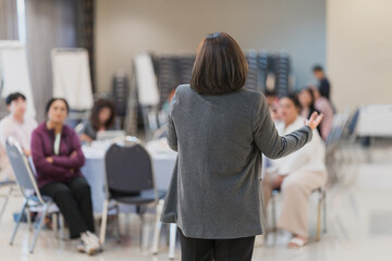 Speaker Leading Business Workshop for Professional Audience. A presenter conducts a business workshop, addressing a group of professionals seated at tables in a modern conference room.