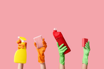 Female hands in rubber gloves with bottles of detergent and sponges on pink background