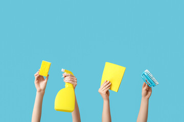 Female hands holding sponge, rag, brush and bottle of detergent on blue background