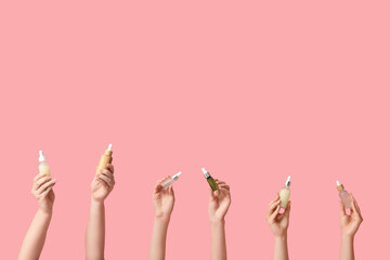Female hands with bottles of different cosmetic products on pink background