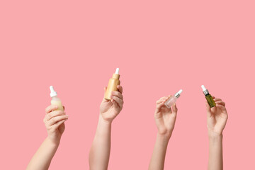 Female hands with bottles of different cosmetic products on pink background