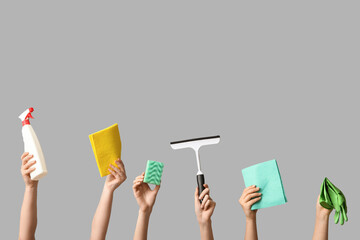 Female hands with sponge, rags, rubber gloves, bottle of detergent and squeegee on grey background