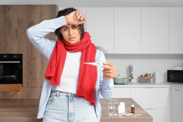 Sick African-American woman measuring temperature at home