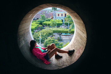 Woman Relaxing in Circular Window Overlooking Lush Park in Granada, Nicaragua