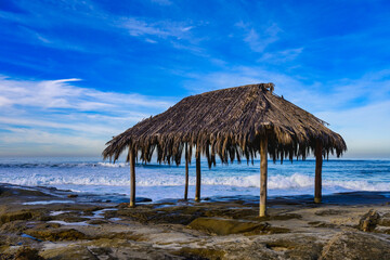  2023-12-31 A GRASS HUT ON A ROCKY SHORLINE WITH WAVES COMING SHORE AT THE WINDANSEA BEACH IN LA...
