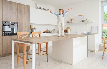 Cute little girl on high table in kitchen. Child at risk