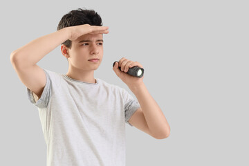 Teenage boy shining flashlight on light background