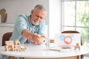 Senior man suffering from Parkinson syndrome at table in kitchen