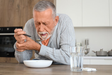 Senior man suffering from Parkinson syndrome eating soup at table in kitchen