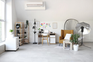 Photographer workplace with armchair, laptop and lighting equipment in modern photo studio