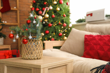 Small Christmas tree with baubles on coffee table in festive living room, closeup