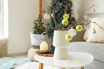 Vase with tree branches and Christmas baubles on coffee table in light living room